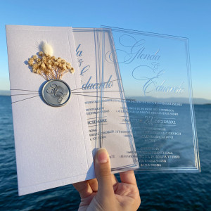 Clear acrylic wedding invitation. White mother-of-pearl half envelope. Silver foil print. Silver wax seal and dried flowers.