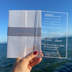 White printed clear acrylic wedding invitation. Parchment wrapping. Belly band with silver foil print. White mailing envelope. 